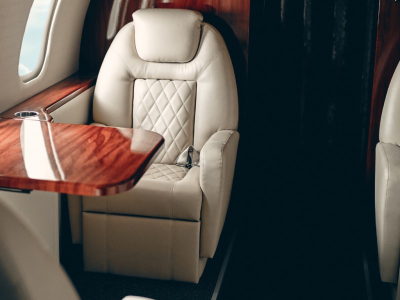 Détail d'un fauteuil en cuir crème et d'une tablette en bois précieux à bord d'un jet privé